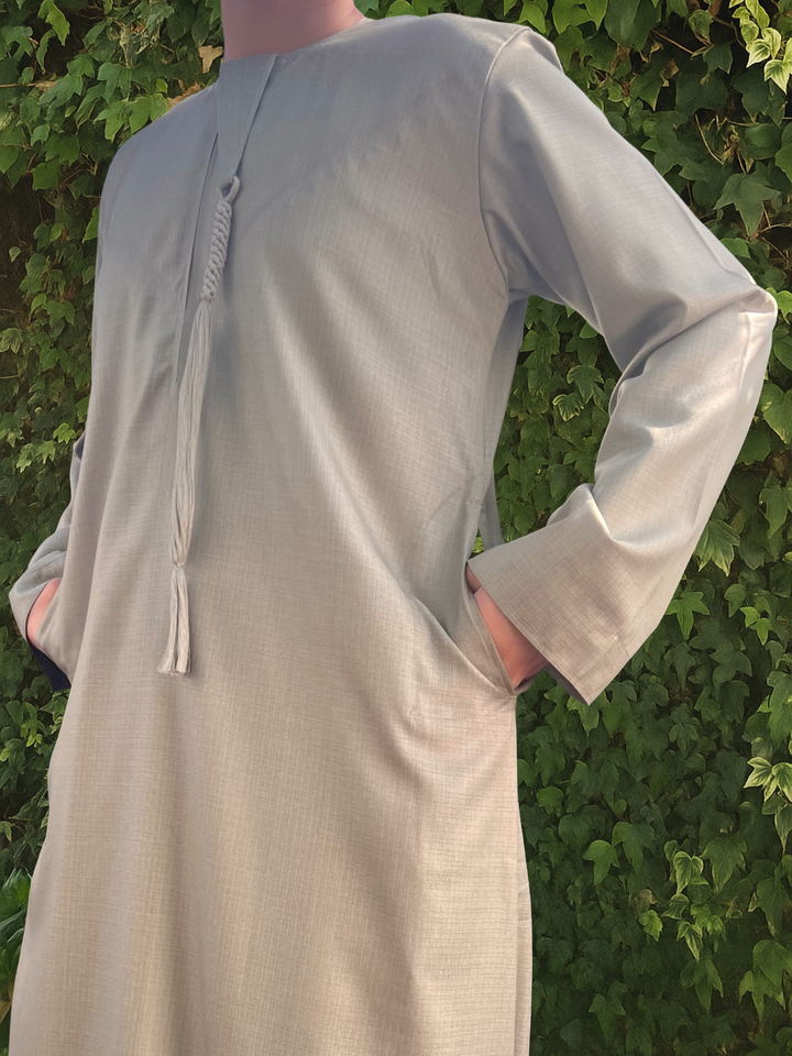 Person wearing a light green long-sleeve thobe against a green leafy background