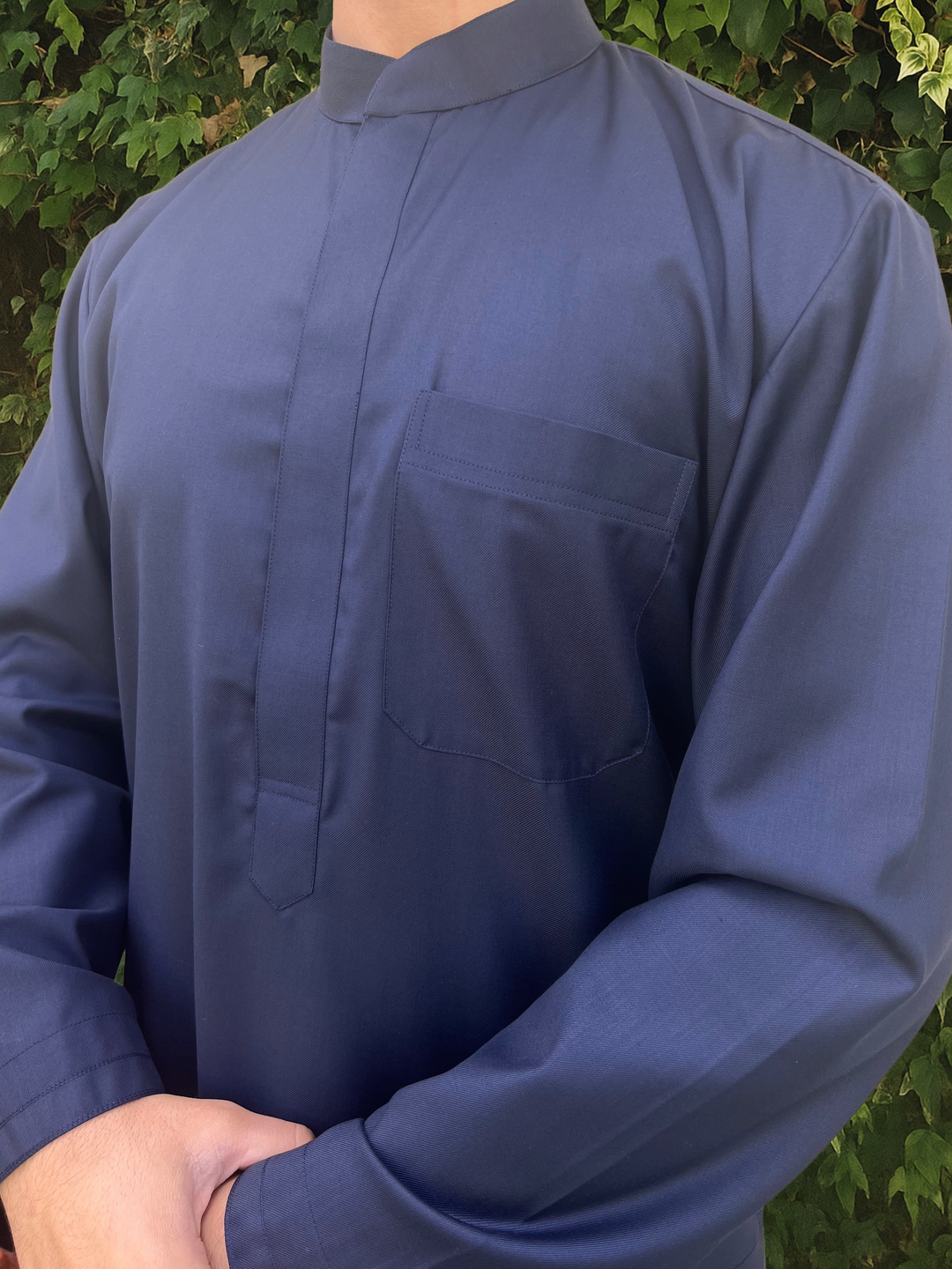 Navy blue long-sleeve collared thobe worn by a person with a green leafy background