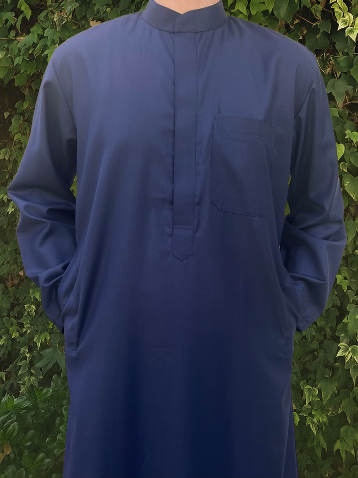 Navy blue long-sleeve collared thobe worn by a man against a green leafy background