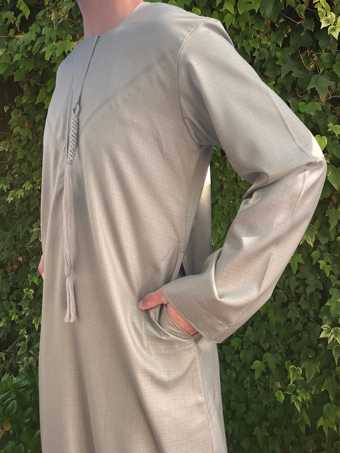 Person wearing a long, light green emirati thobe against a green leafy background