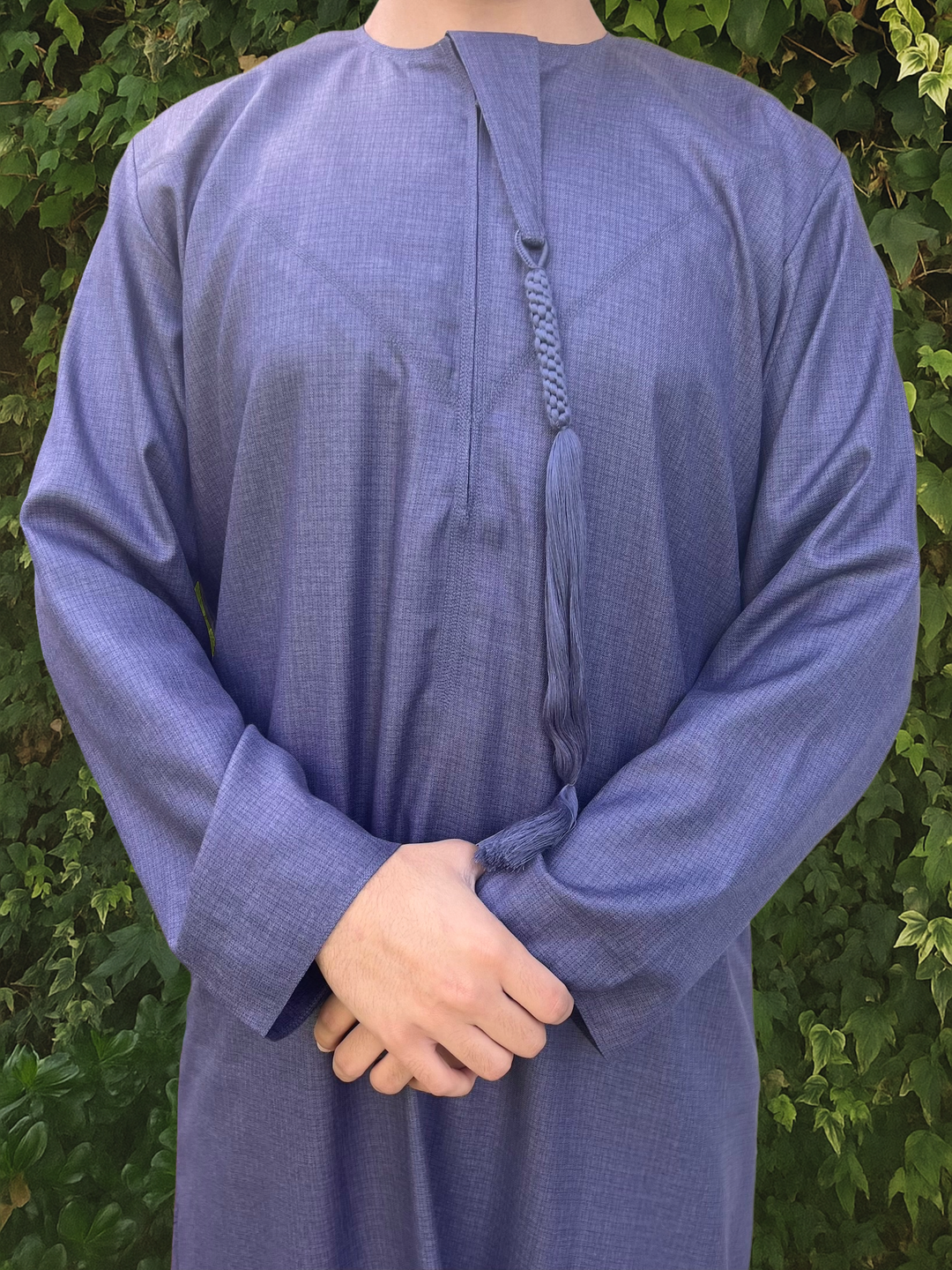 Person wearing a blue traditional outfit/thobe with a green leafy background