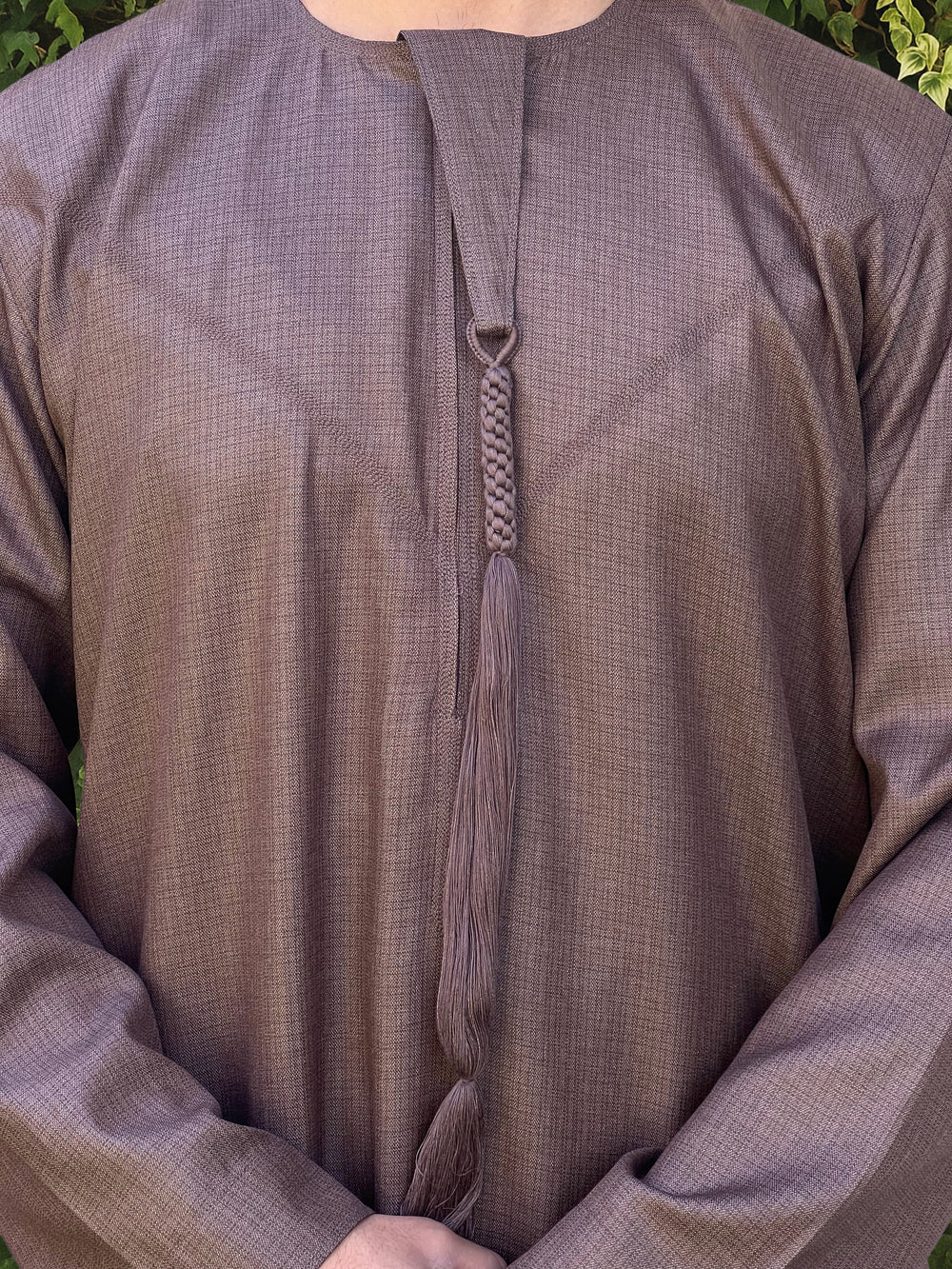 Close-up of a brown textured thobe with a emirati tassel detail.