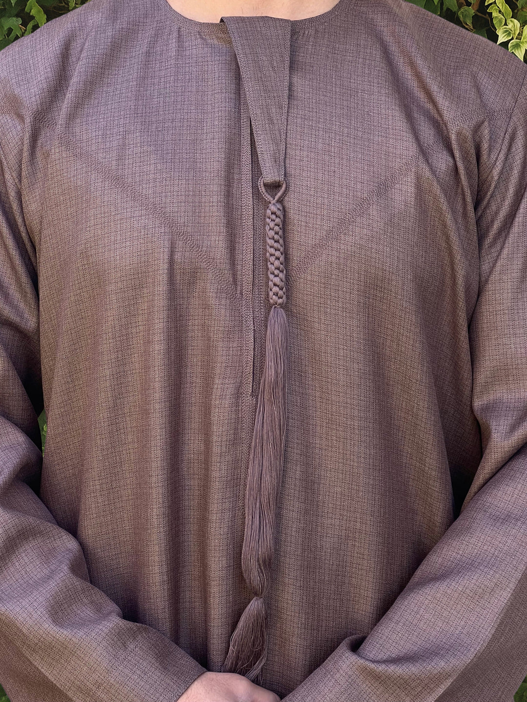 Close-up of a brown textured thobe with a emirati tassel detail.