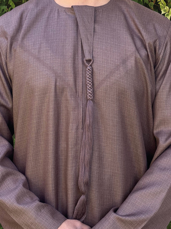 Close-up of a brown textured thobe with a emirati tassel detail.