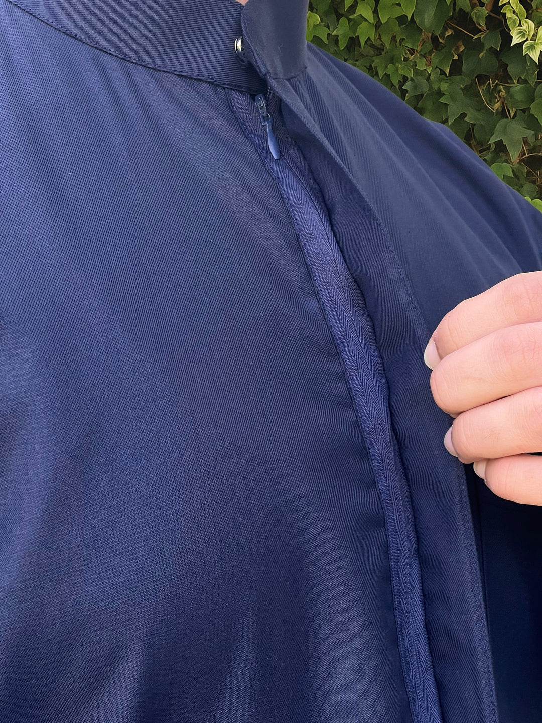 Close-up of a person wearing a navy blue thobe with a blurred green background